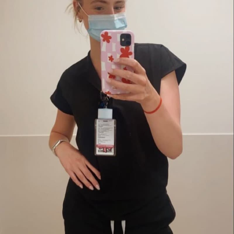 Nursing student in scrubs taking a mirror selfie with her hospital ID badge